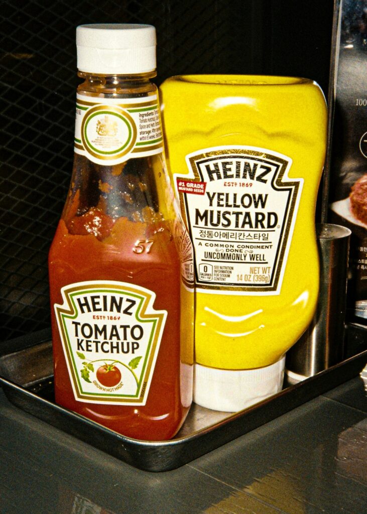 A bottle of Heinz Tomato Ketchup in front of a bottle of Heinz Yellow Mustard